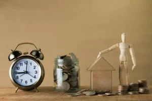 A picture of a clock, some coins in a jar, and a wooden figurine with a wooden house.